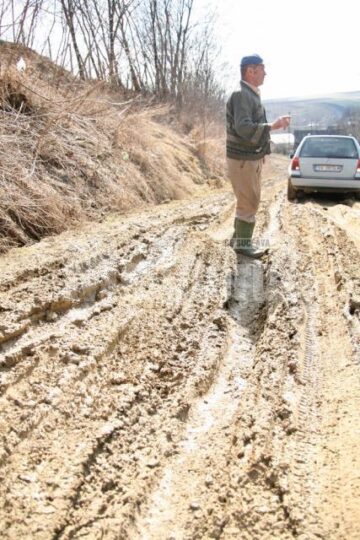 O masina pe drumul desfundat si un satean in obligatoriile cizme