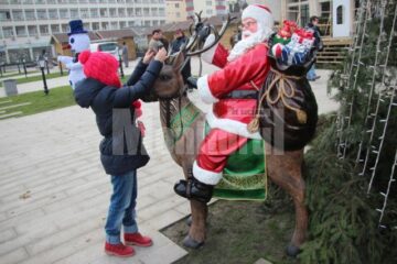 Moș Crăciun și Omul de zăpadă îi așteaptă pe copii lângă bradul de Crăciun