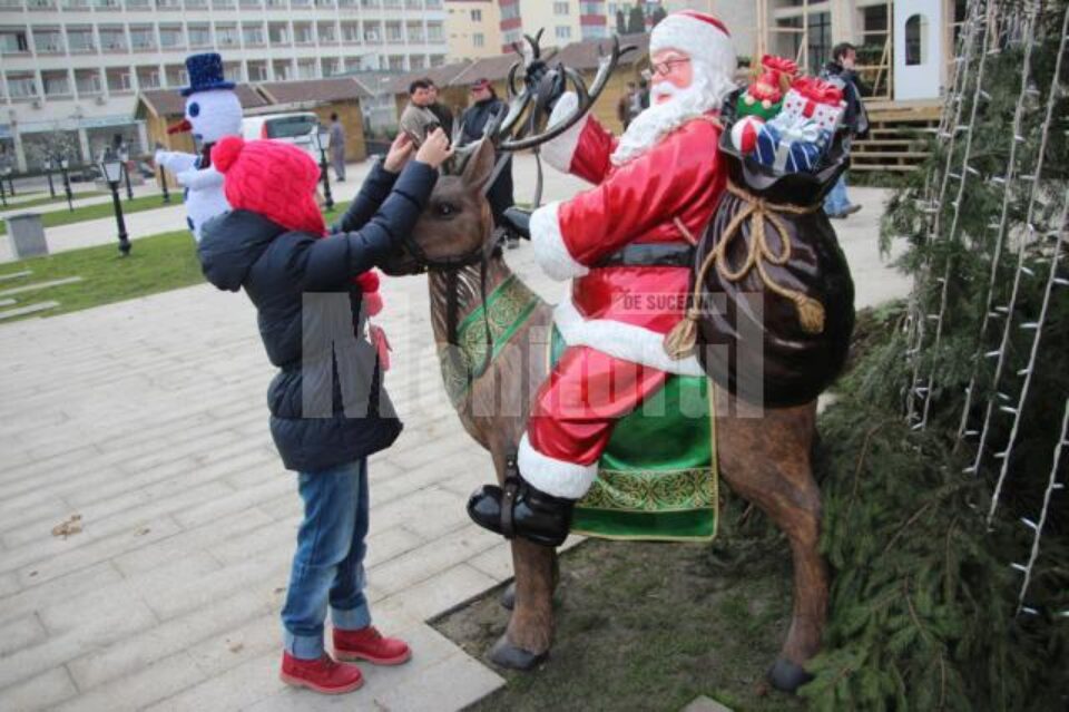Moș Crăciun și Omul de zăpadă îi așteaptă pe copii lângă bradul de Crăciun
