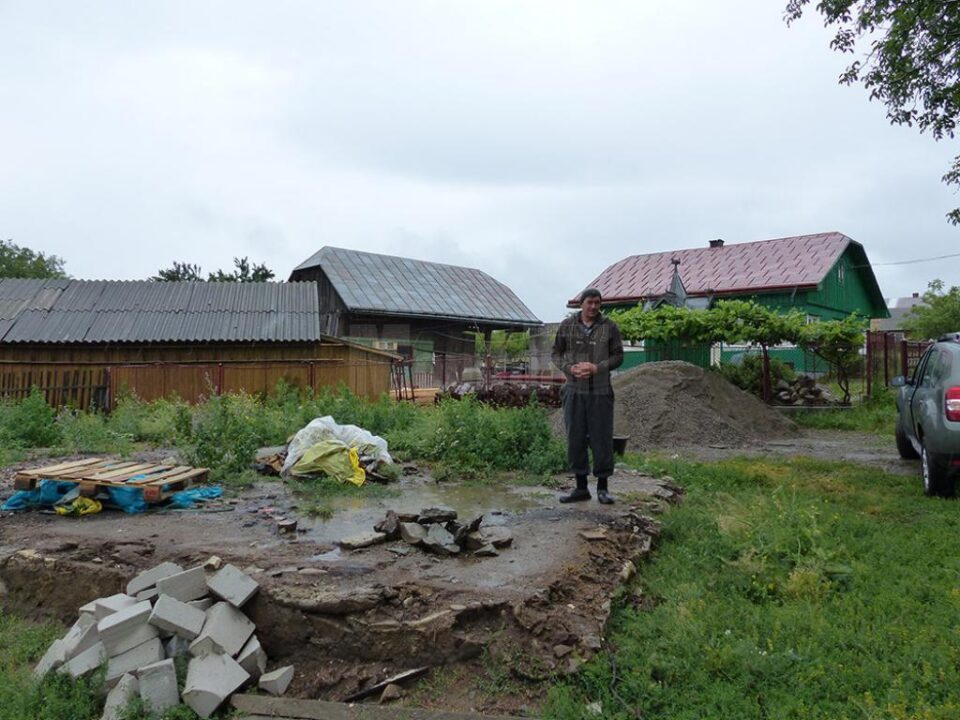 Relu Baciu, pe locul unde a fost casa sa. În plan îndepărtat este actuala sa casă, pe care a cumpărat-o din donațiile oamenilor de bine