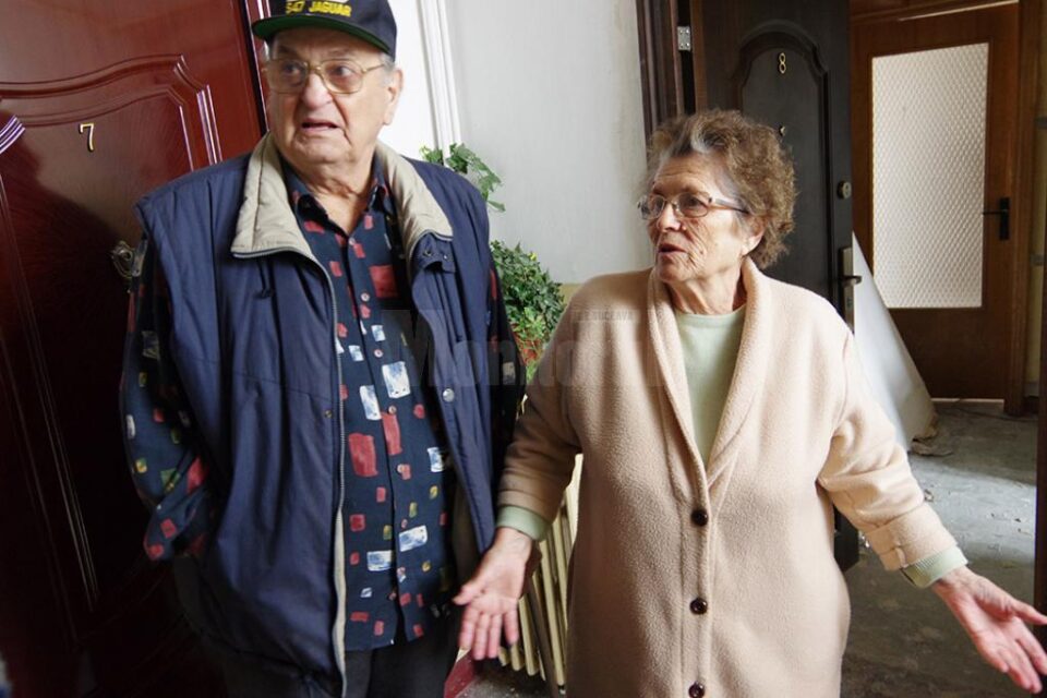 Cei doi bătrâni stau cu cearșaf în geam, în așteptarea tâmplăriei noi, pentru care au achitat deja peste 6.000 de lei