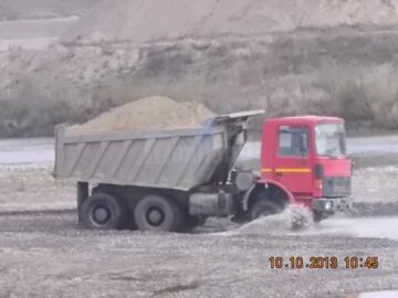 Camioanele firmei, transportând balastul prin apa râului, spre celalalt mal