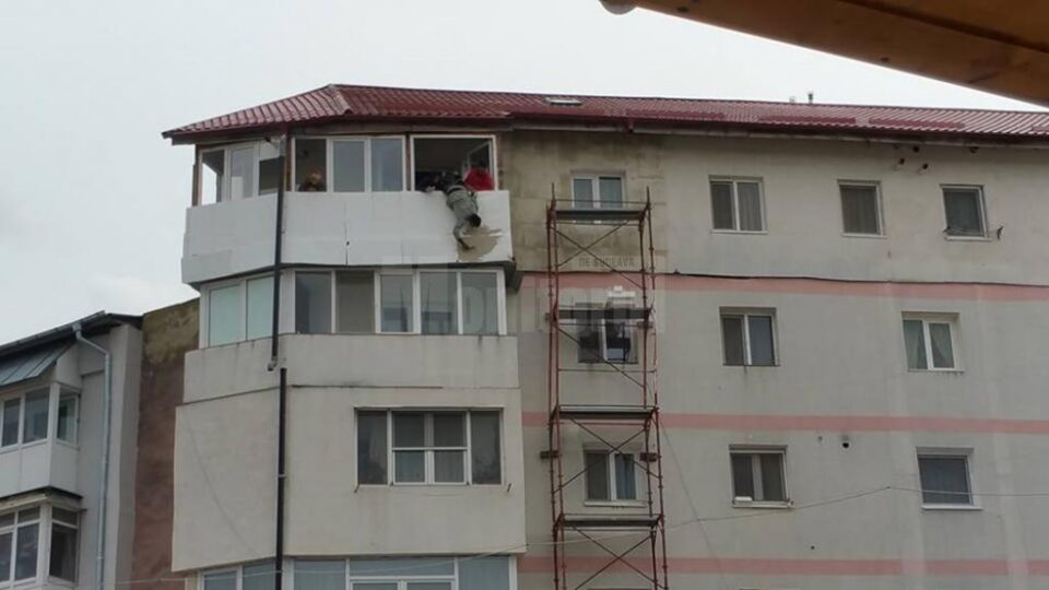 "Batman"-ul Dorel, lucrând la izolarea termică a unui balcon aflat la etajul cinci al clădirii, ținut de haină de un coleg