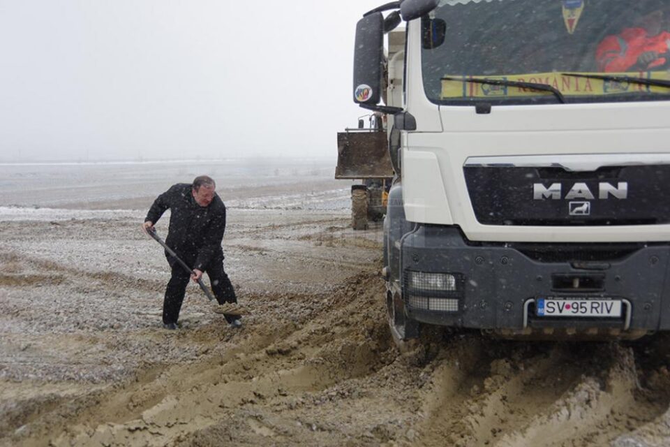 Președintele CJ dând cu lopata pietriș sub roțile unei basculante care patina și nu mai putea înainta