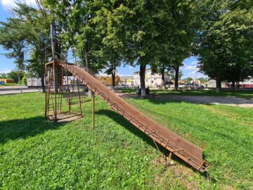 Un tobogan metalic, ruginit, stă abandonat în curte